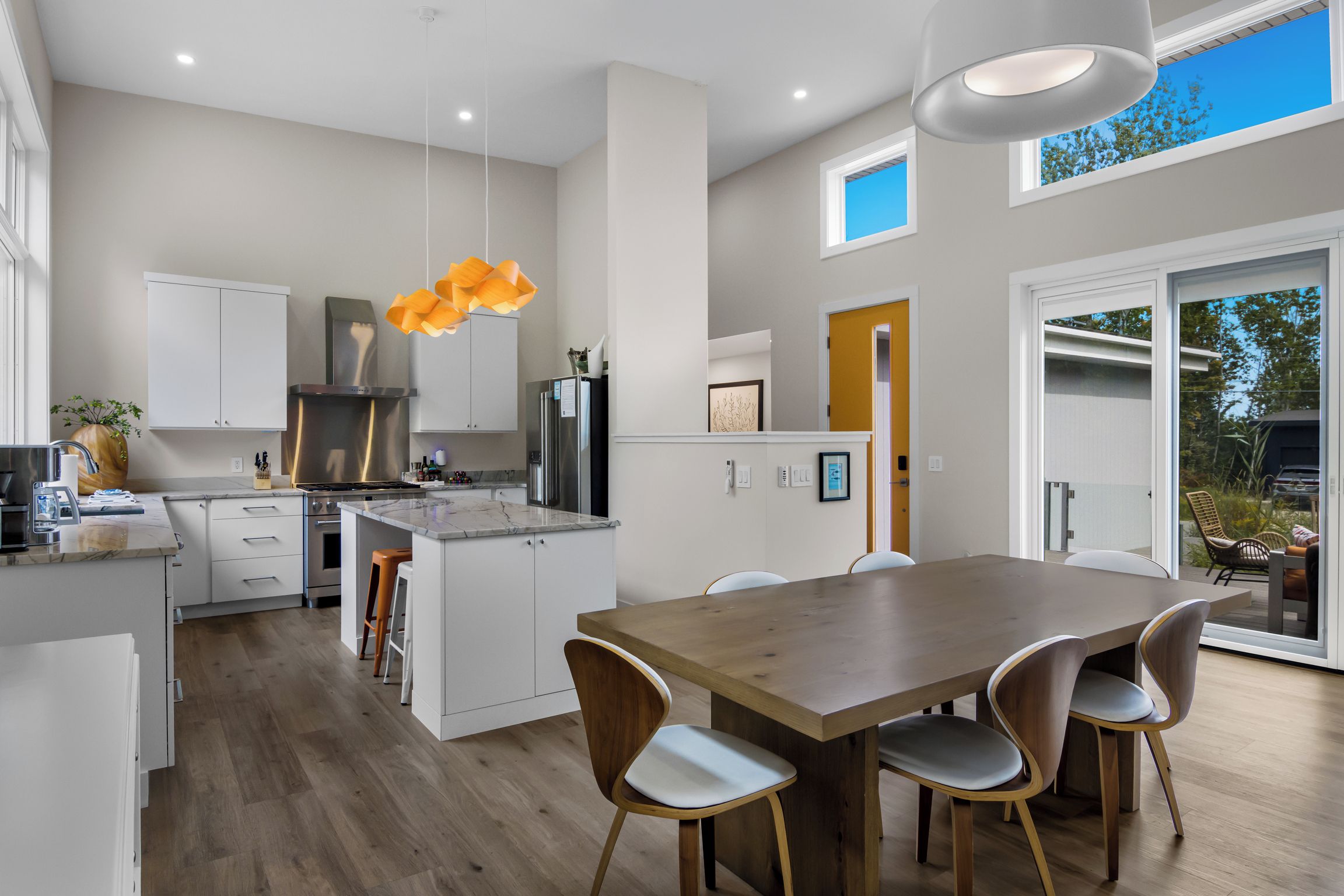 A modern kitchen with white cabinetry, stainless steel appliances, and a wooden dining table with chairs.