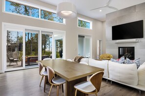 Ein modernes Wohnzimmer mit Essbereich, großen Fenstern und einem Kamin.