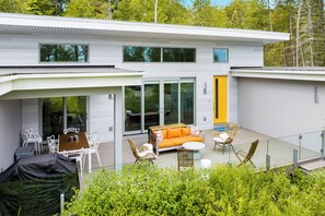 Una casa moderna de dos pisos con un patio cubierto que incluye mobiliario exterior y una mesa de comedor.
