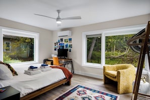 A bedroom with a bed, a desk, a chair, a television, and large windows. - Stargazer – Modern Luxury Meets Up North Charm (Northport)