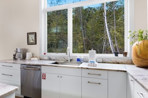 A modern kitchen with a large window, a dishwasher, and a fire exit sign. - Stargazer – Modern Luxury Meets Up North Charm (Northport)