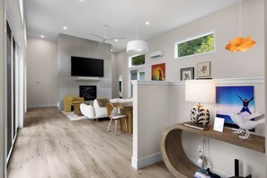 A modern living room with a flat-screen TV, a fireplace, a sofa, and a dining area with a wooden table. - Stargazer – Modern Luxury Meets Up North Charm (Northport)