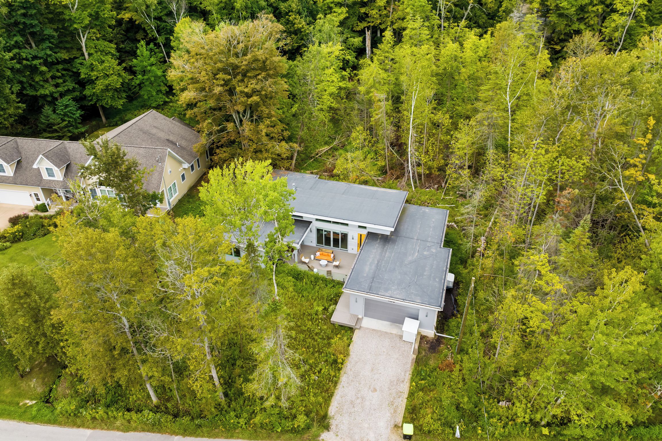 A modern two-story house with a covered patio and a garage, surrounded by dense trees.