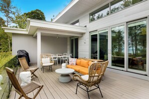 An outdoor deck with a dining set, seating area, and a barbecue grill. - Stargazer – Modern Luxury Meets Up North Charm (Northport)