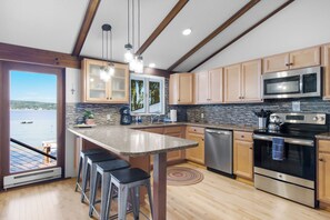 A modern kitchen with a large island, stainless steel appliances, and a view of the water.