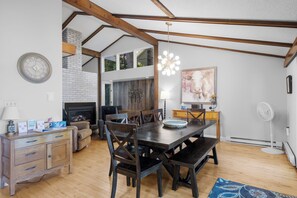 A dining area with a wooden table and chairs, a fireplace, and a modern chandelier.