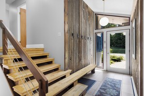 A wooden staircase leading to a door with a view of greenery outside.