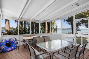 A covered outdoor seating area with a table and chairs, overlooking a body of water.