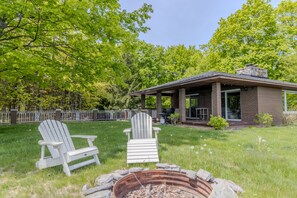 A house with a covered patio, two Adirondack chairs, and a fire pit. - Violet’s View — Where Pets & People Vacation (Suttons Bay)