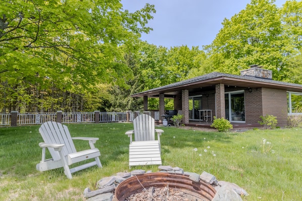 A house with a covered patio, two Adirondack chairs, and a fire pit.