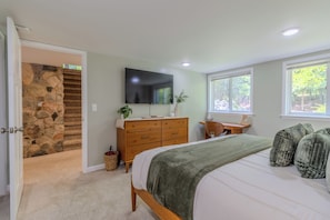 A bedroom with a stone staircase, a wooden dresser, a bed with a green blanket, and a TV on the wall. - Violet’s View — Where Pets & People Vacation (Suttons Bay)