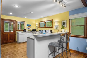 A kitchen with a central island, bar stools, wooden flooring, and a door. - Wild Things Cottage Near Sleeping Bear Dunes (Empire)