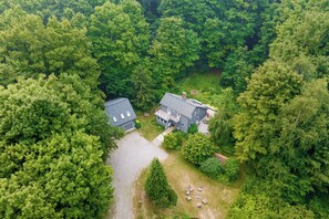 A two-story house surrounded by dense forest, with a visible driveway and outdoor seating area. - Wild Things Cottage Near Sleeping Bear Dunes (Empire)