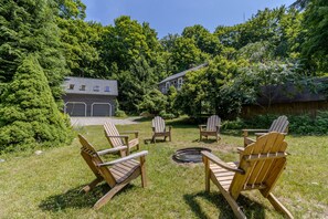 Ein Garten mit Holz-Adirondack-Stühlen um ein Feuerkörbchen, umgeben von üppiger Bepflanzung und einem Holzzaun.
