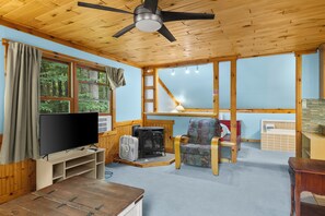 Une pièce confortable avec une télévision, une cheminée, un fauteuil et un ventilateur de plafond.