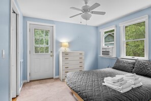 Un dormitorio con cama, cómoda, ventilador de techo y ventana con vista a follaje.