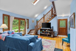 Un salon avec un canapé bleu, un téléviseur posé sur un meuble en bois et un escalier.