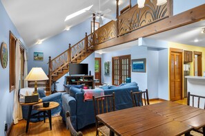 A cozy living room with a wooden staircase, a television, and a dining table. - Wild Things Cottage Near Sleeping Bear Dunes (Empire)