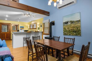 Un comedor con mesa y sillas de madera, una cocina con barra y un cuadro en la pared.