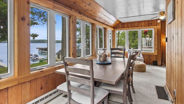 A wooden deck with a dining table, chairs, and a view of a lake. - Cozy Cottage on Long Lake, Your Perfect TC Getaway (Traverse City)