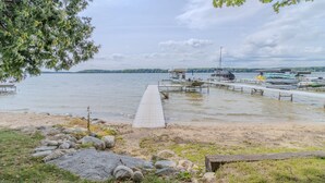 A lakeside dock with boats, a wooden pier, and a grassy area with rocks. - Cozy Cottage on Long Lake, Your Perfect TC Getaway (Traverse City)