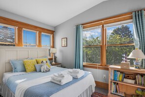 A bedroom with a bed, pillows, a bedside table with a lamp, a bookshelf, and a window with curtains. - Welcome to All-Seasons Downtown Beulah Beauty! (Beulah)