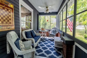 A covered porch with wicker furniture, a chessboard, and a view of a grassy area with an American flag. - Welcome to All-Seasons Downtown Beulah Beauty! (Beulah)