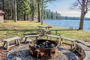 A lakeside campsite with a fire pit, picnic tables, and a view of the lake.