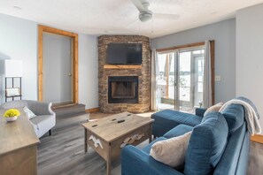 A living room with a stone fireplace, a flat-screen TV, a wooden coffee table, and a blue sofa.