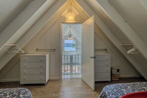 Un dormitorio en el ático con techo inclinado, paredes de madera y vistas al exterior a través de una puerta.
