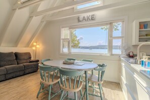 Un acogedor comedor con una mesa redonda y sillas a juego, una ventana con vistas a un lago, y un letrero sobre la ventana que dice "LAKE".