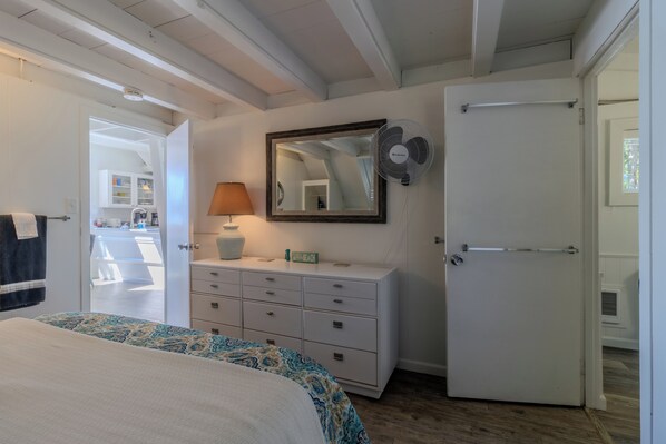 Un dormitorio con cama, cómoda, espejo, ventilador y puerta.