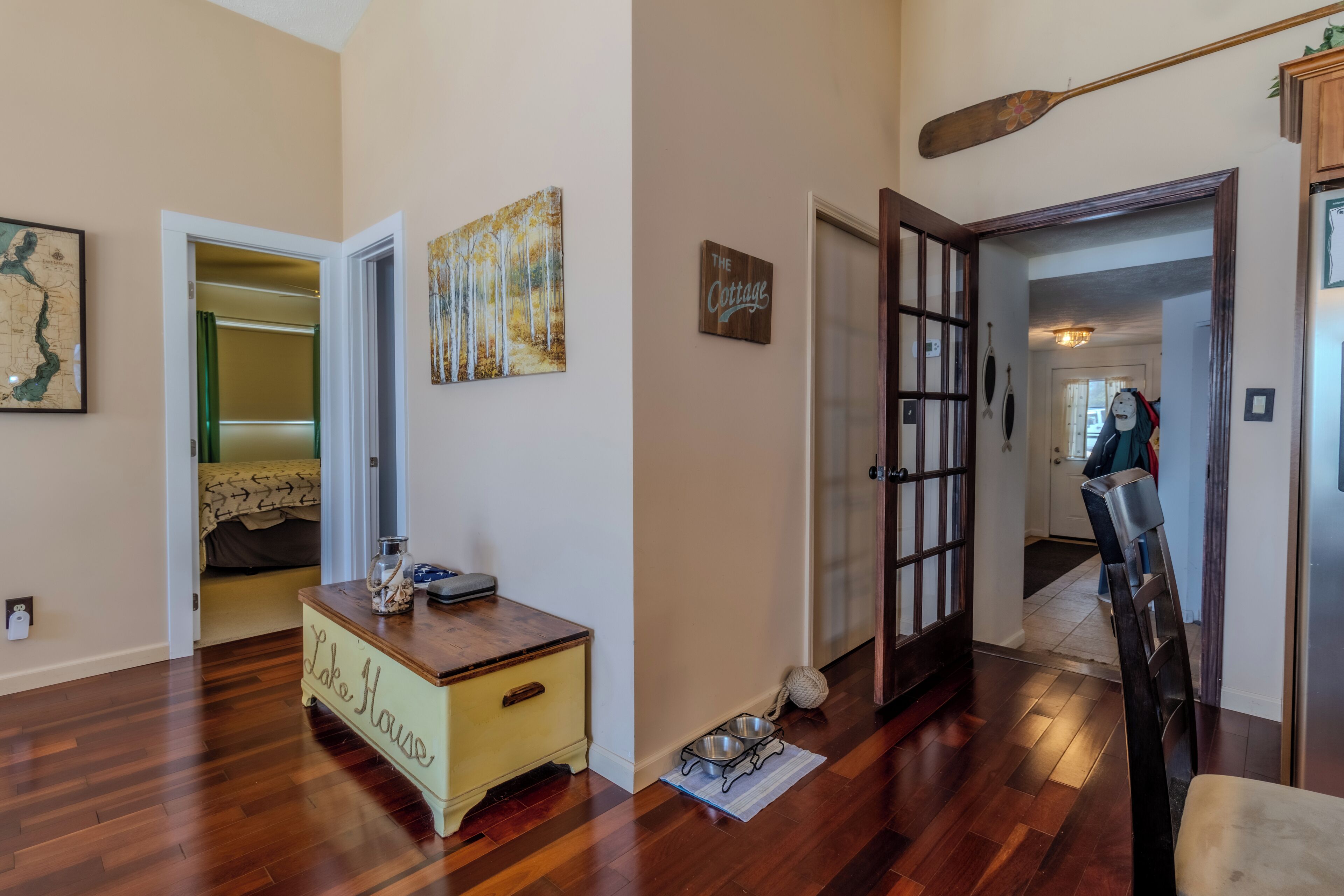 A hallway with wooden flooring, a coat rack, a door with a glass panel, and a sign that reads "The Cottage."