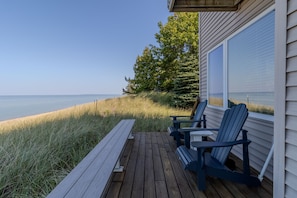 A wooden deck with two Adirondack chairs and a bench overlooking a beach.