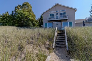A two-story house with a balcony, surrounded by tall grass and trees.
