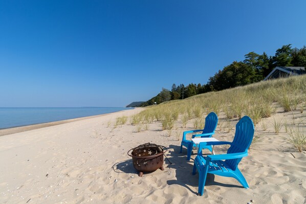 A beach with two blue chairs and a star-shaped metal pot.