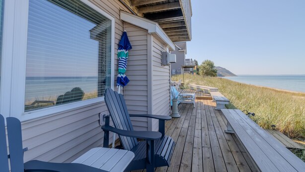 A wooden deck with outdoor furniture, a view of the beach, and a house with a window overlooking the ocean. - Tranquil beachfront studio at Sunset Suite (Empire)