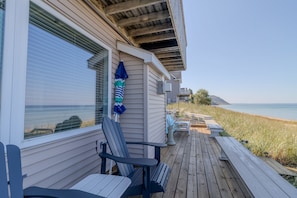 Una terraza de madera con mobiliario exterior, vistas a la playa y una casa con ventana que da al océano.