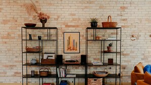 A room with a brick wall, two black metal shelving units, a framed artwork, and a patterned rug.