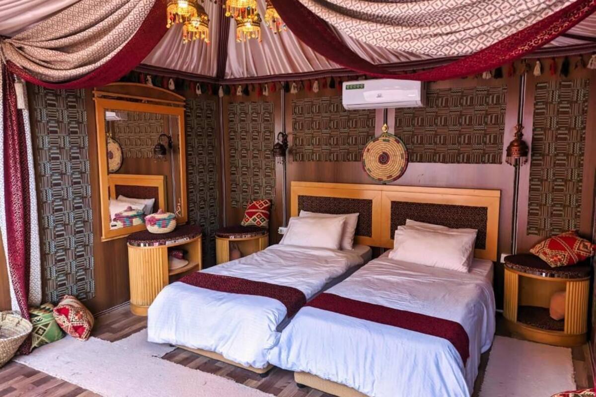 Una habitación con dos camas, paredes con diseño, un espejo y un ventilador de techo.