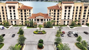 A large hotel with a central courtyard, multiple parking spaces, and a view of a body of water.