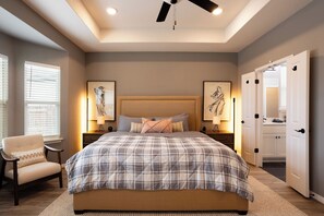 Une chambre à coucher avec un grand lit, deux tables de chevet, une chaise et un ventilateur de plafond.