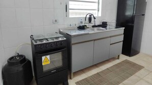 A kitchen with white tiled walls, a window, a black stove, a black refrigerator, and a sink. - Brisa e Mar Townhouse (Caraguatatuba)
