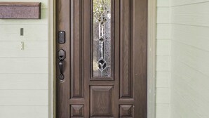Una porta d'ingresso marrone con un pannello in vetro, un tappetino da porta con la scritta 'HOME' e un lampadario fissato al muro.