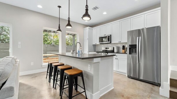 A modern kitchen with white cabinets, a stainless steel refrigerator, a microwave, and a bar area with stools. - Modern East Austin Home – Walk to Downtown! (Austin)