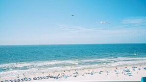 A beach with people, umbrellas, and a plane in the sky. - Wraparound Balcony, Corner 3 BR Condo w Direct Beach Access (Orange Beach)