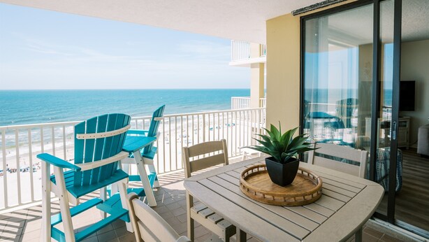 A balcony with a view of the ocean, a table with chairs, and a potted plant. - Wraparound Balcony, Corner 3 BR Condo w Direct Beach Access (Orange Beach)