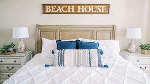 A bedroom with a bed, two bedside tables, a wall-mounted sign, and a nightstand with a lamp. - Wraparound Balcony, Corner 3 BR Condo w Direct Beach Access (Orange Beach)