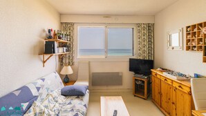 Ett rum med en soffa, ett soffbord, en tv, en bokhylla och ett fönster med utsikt över havet.
