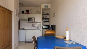 Kompakti keittiö, jossa on mikroaaltouuni, liesi ja pieni jääkaappi. Keittiössä on ruokapöytä, jonka päällä on sininen pöytäliina ja kynttilänjalka.